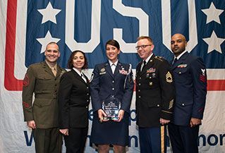 A group of people in military uniforms are standing in front of an american flag.