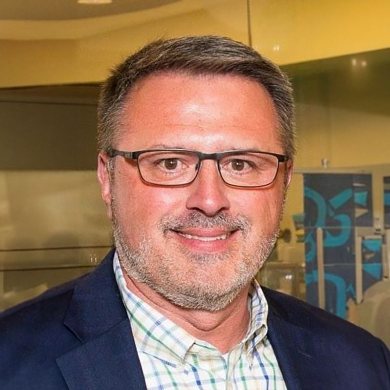 A man wearing glasses and a suit is smiling for the camera.