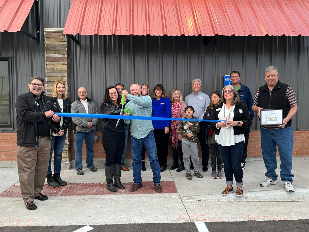 A group of people are cutting a blue ribbon in front of a building.