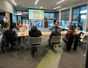 A group of people are sitting at tables in a room watching a presentation.