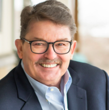 A man wearing glasses and a suit is smiling for the camera