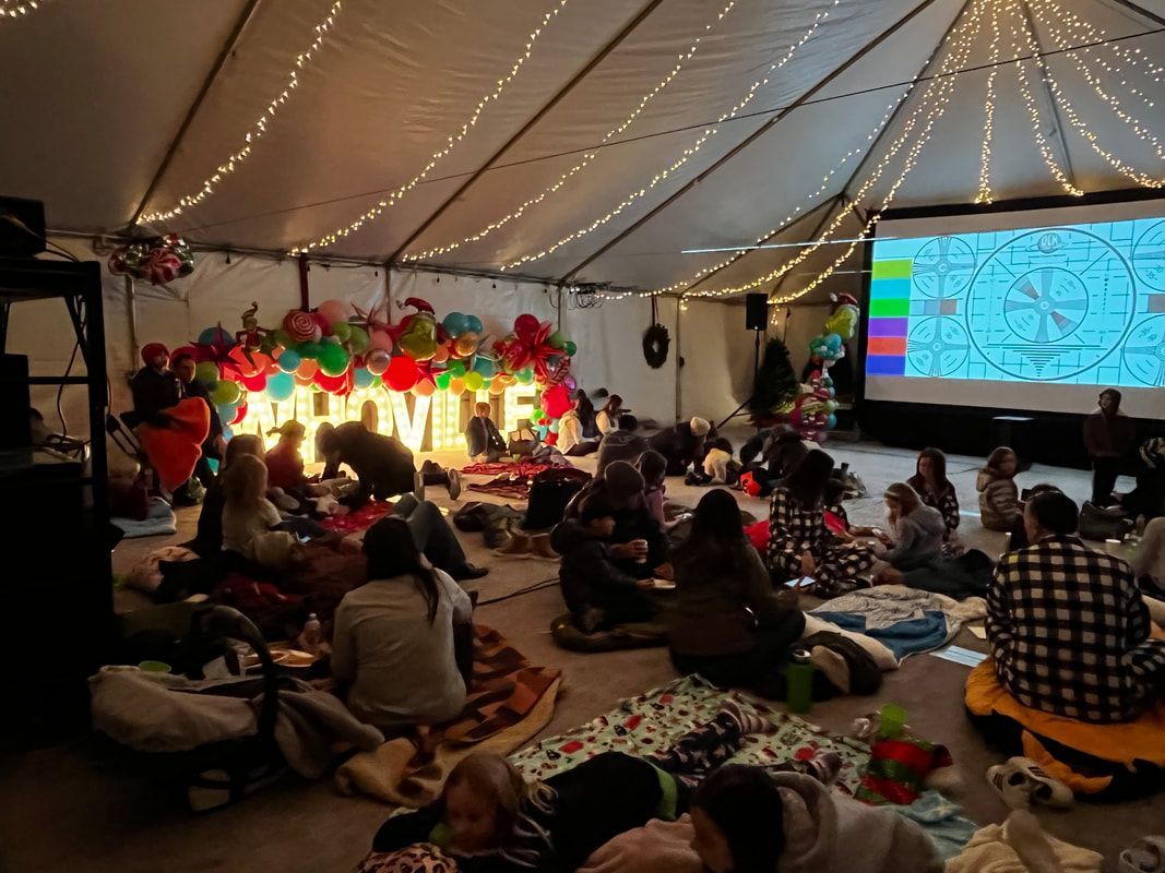 A group of people are sitting under a tent watching a movie.