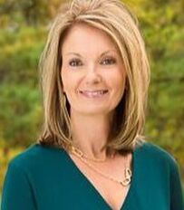 A woman wearing a green shirt and a gold necklace is smiling for the camera.