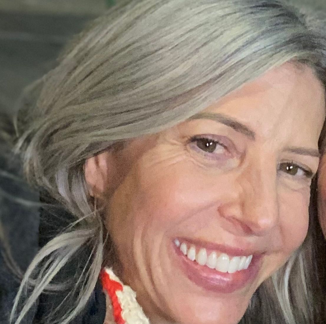 A woman in a black sweater is smiling in front of a tree.