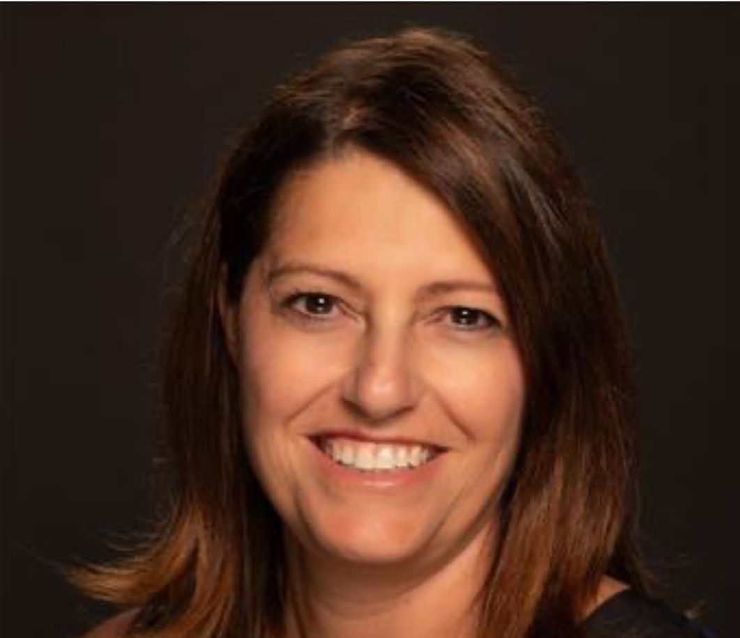 A woman with long brown hair is smiling for the camera.