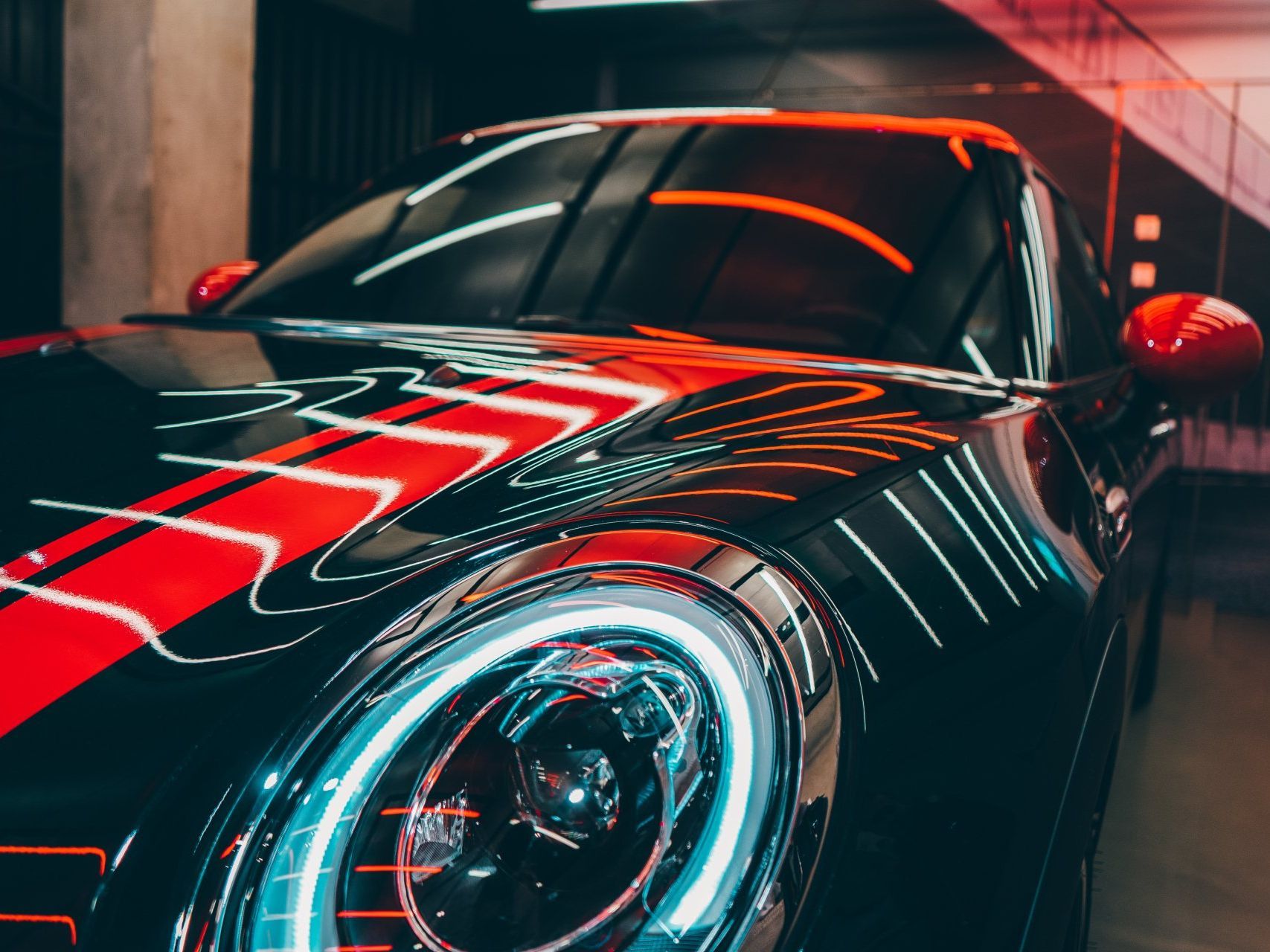 A black sports car with bright red racing stripes and glowing, blue-ringed headlights in a dimly lit garage.