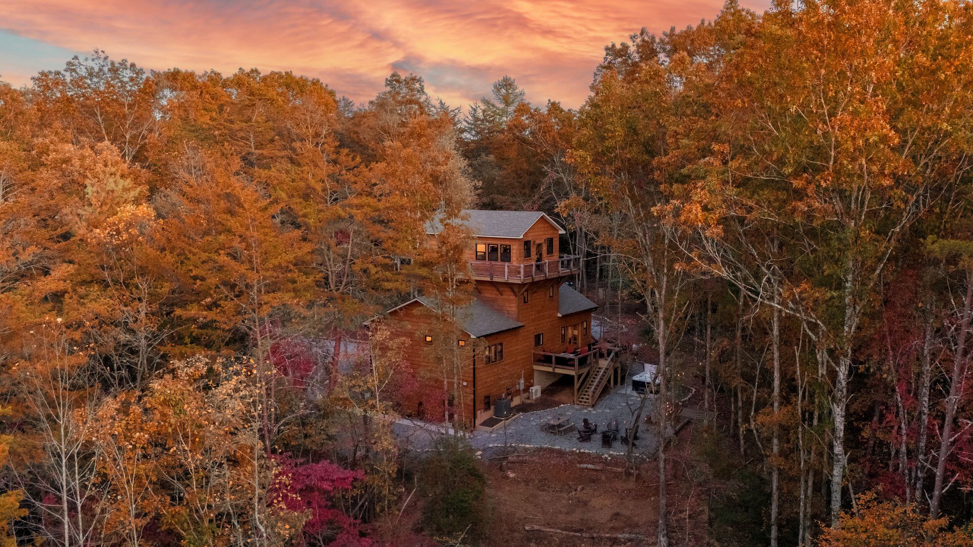 Rustic cabin nestled among autumn trees under a warm sunset sky