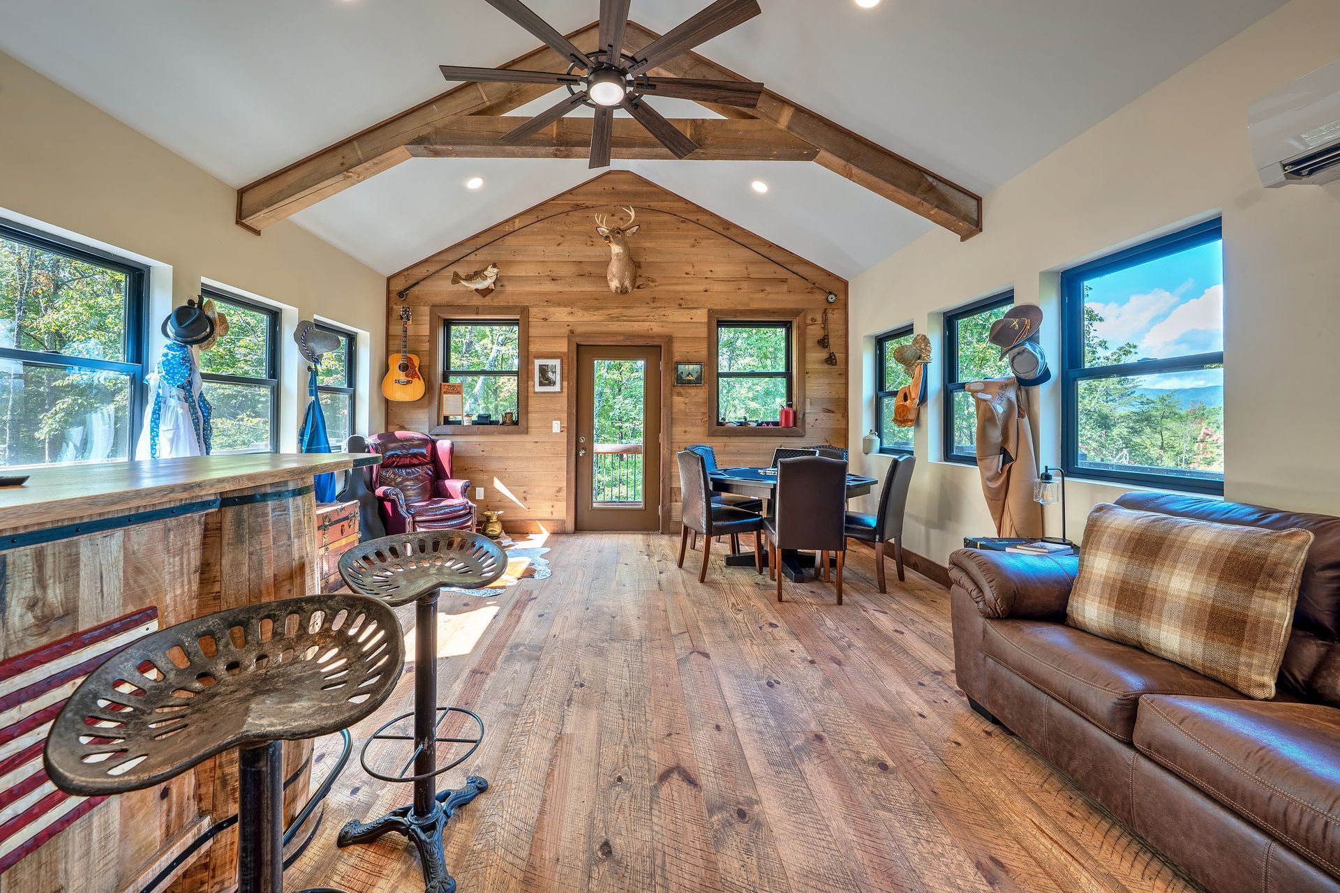 Cozy modern cabin living room with wood beams, large windows, leather sofa, and dining table.