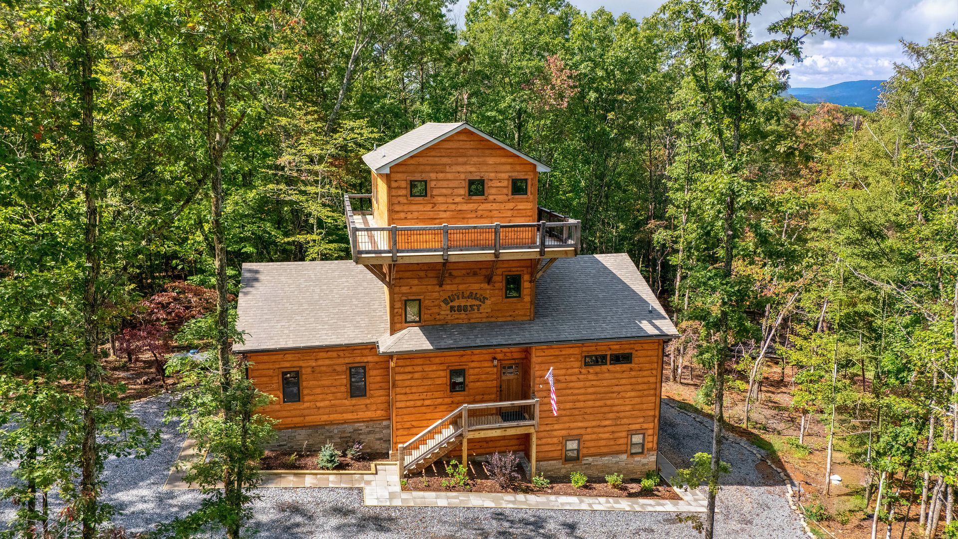 Wooden cabin in a wooded area with a balcony, gray roof, and surrounding trees