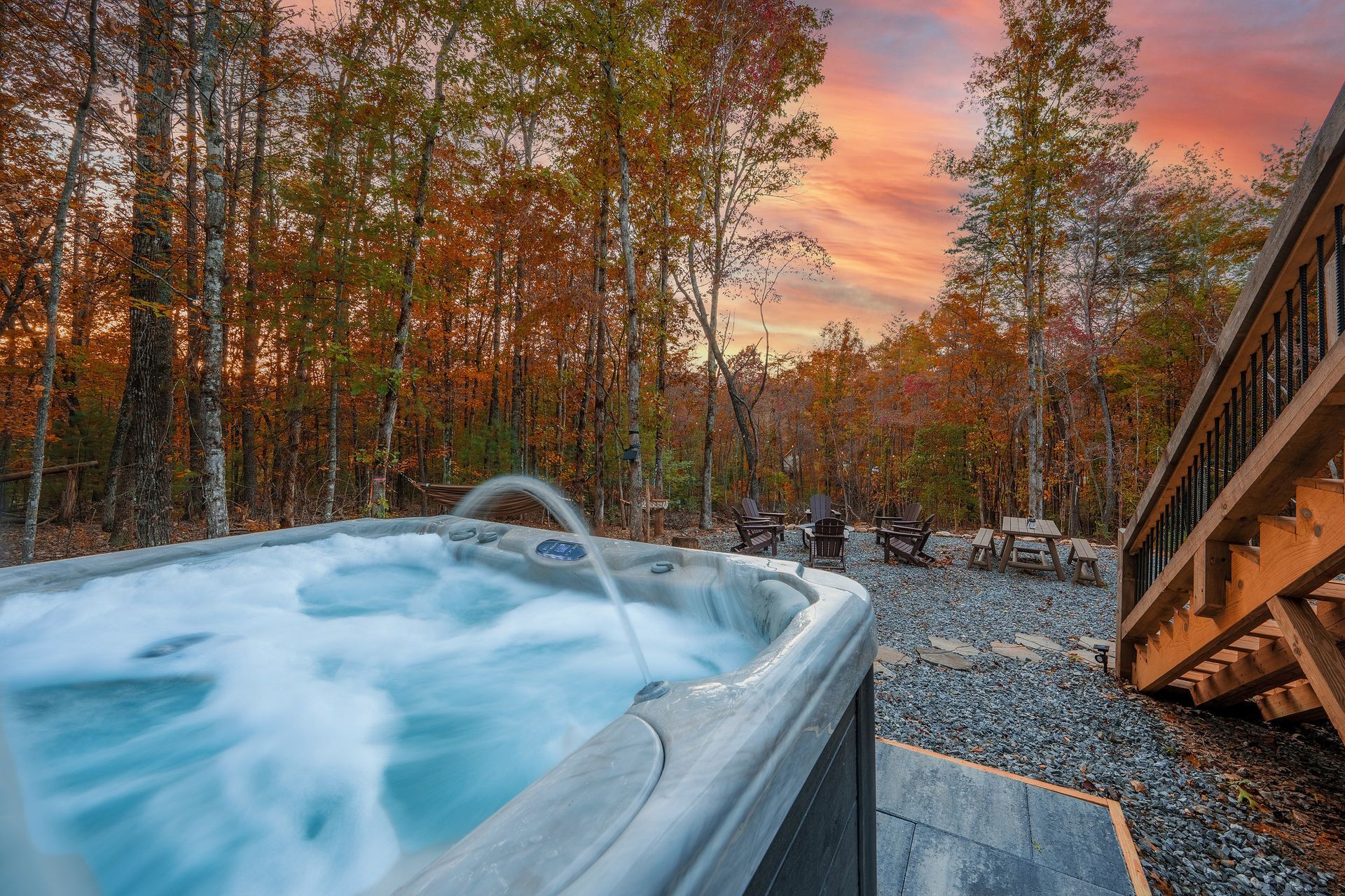 Hot tub steaming at sunset beside a forest and wooden deck stairs