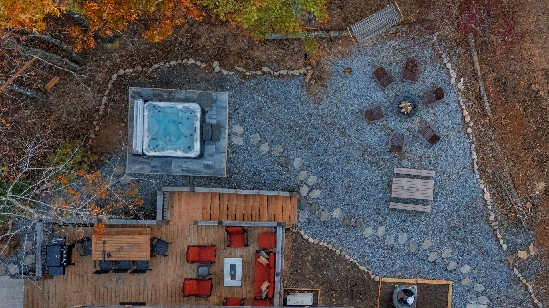 Aerial view of a wooden deck beside a gravel patio with a square hot tub and outdoor seating