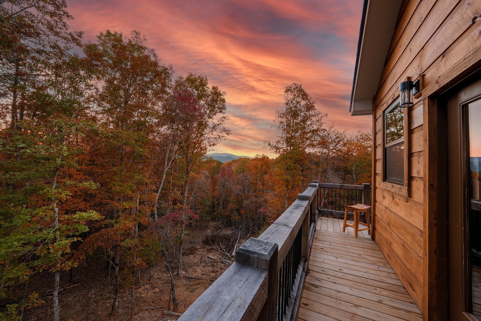 Wooden deck overlooking autumn trees at sunset, with a warm orange sky.