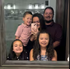 Family of four taking a mirror selfie indoors, smiling in a dimly lit room.