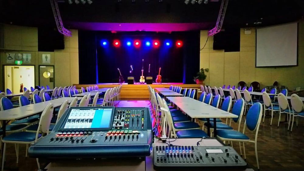An Empty Auditorium With Tables and Chairs and a Stage With Purple Lights — Inspired Audio Visual in Coffs Harbour, NSW