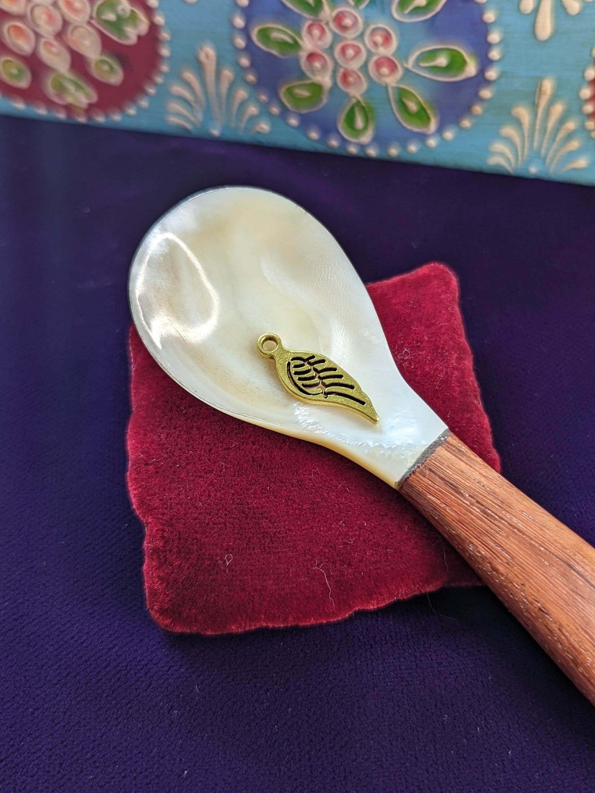 single feather charm on shell spoon sitting on a miniature velvet pillow