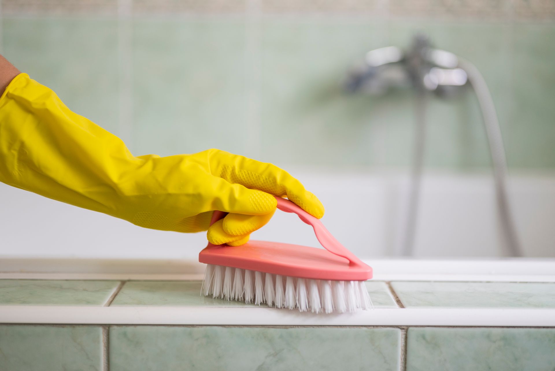 A person wearing yellow rubber gloves is cleaning a bathtub with a brush.