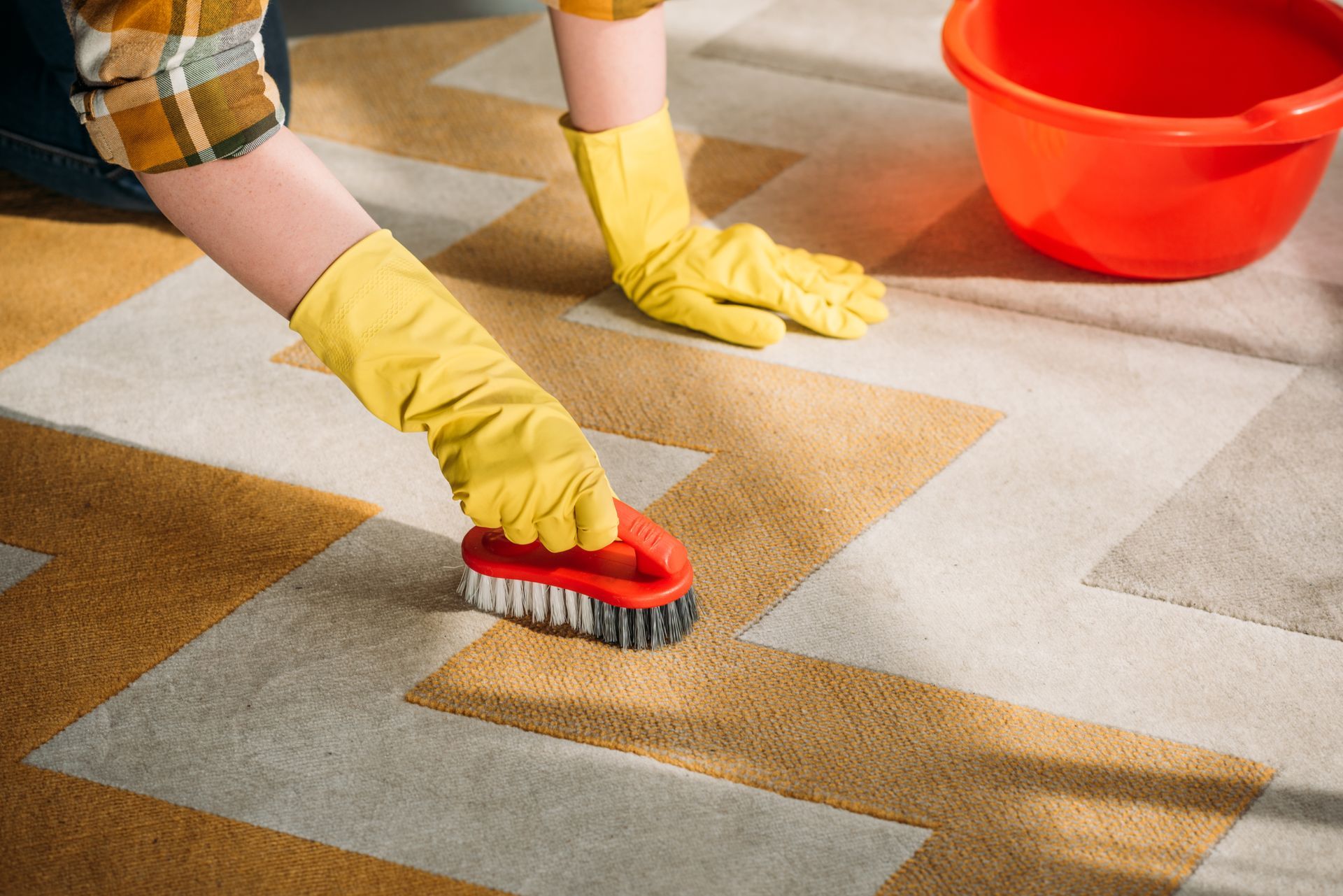 A person wearing yellow gloves is cleaning a rug with a brush.