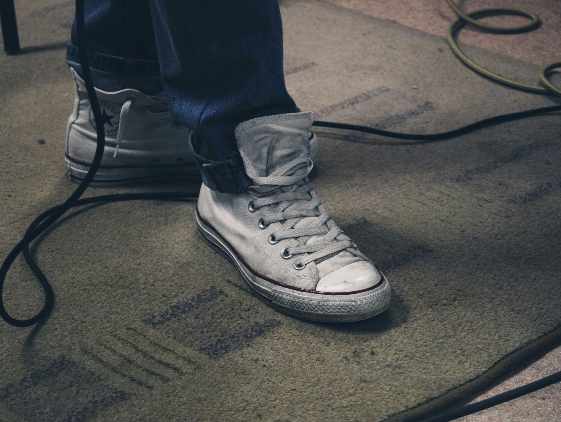 A person wearing white sneakers is standing on a rug next to a microphone.