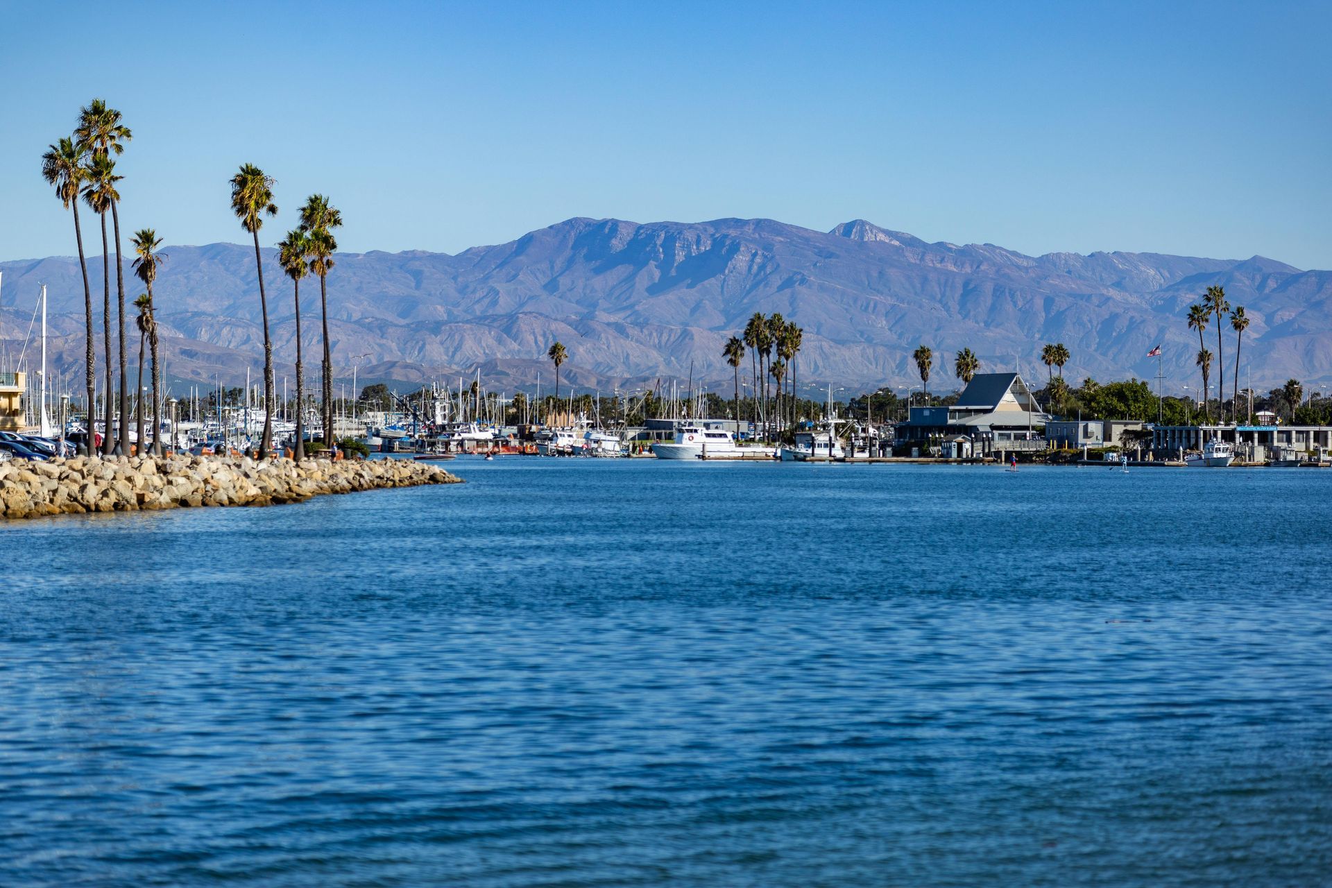 A body of water with mountains in the background and palm trees in the foreground.