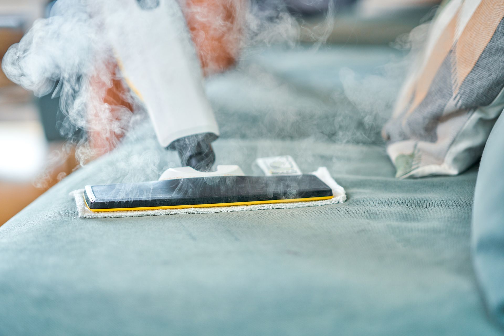 A person is using a steam mop to clean a couch.