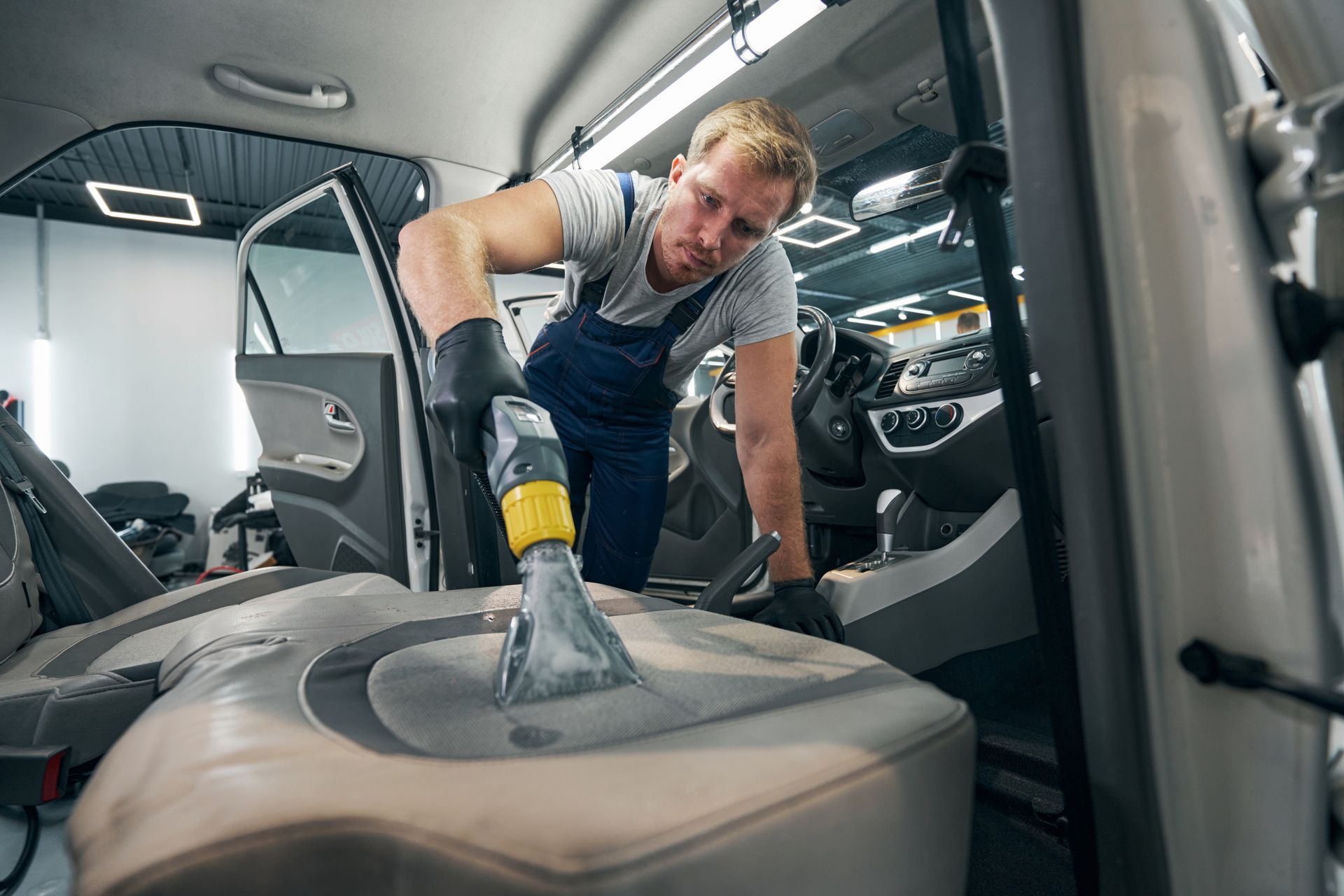 A man is cleaning the seats of a car with a vacuum cleaner.