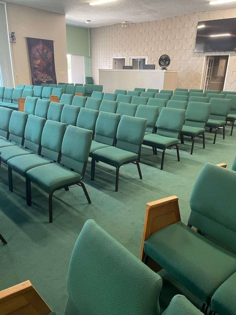 Rows of green chairs are lined up in a large auditorium.