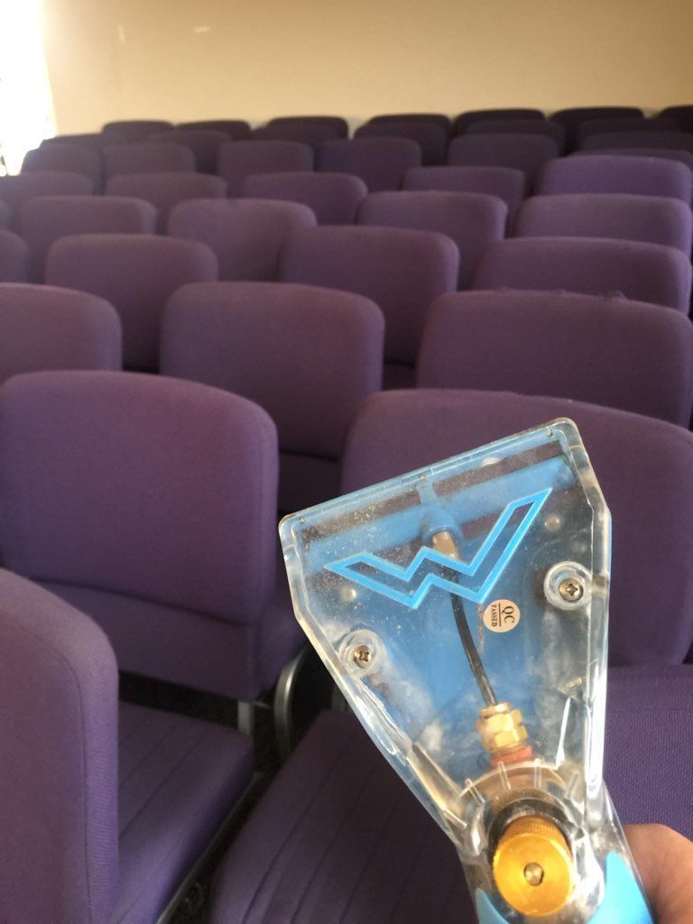 A person is holding a vacuum cleaner in front of a row of purple chairs
