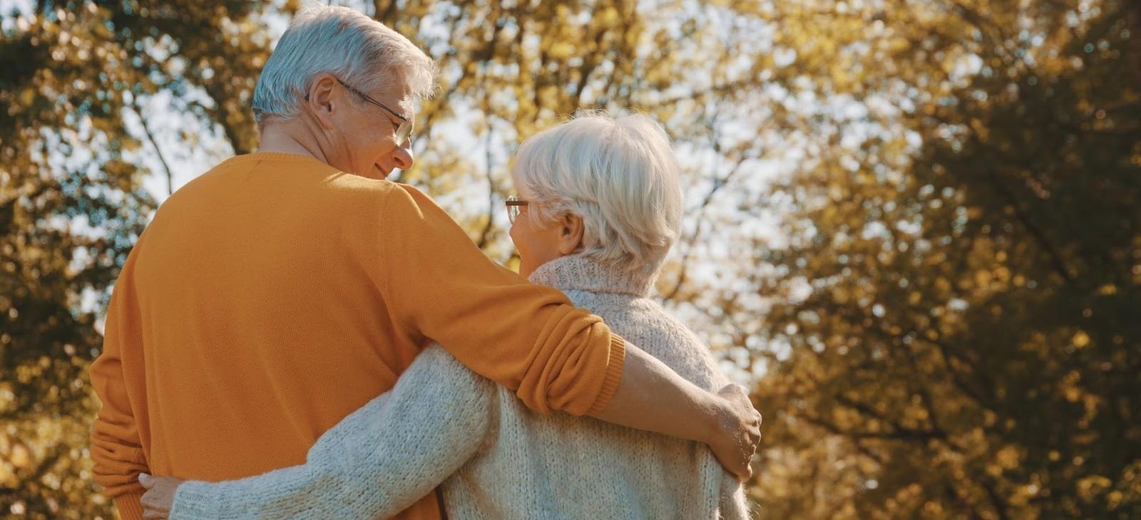 an elderly couple is hugging each other in a park .