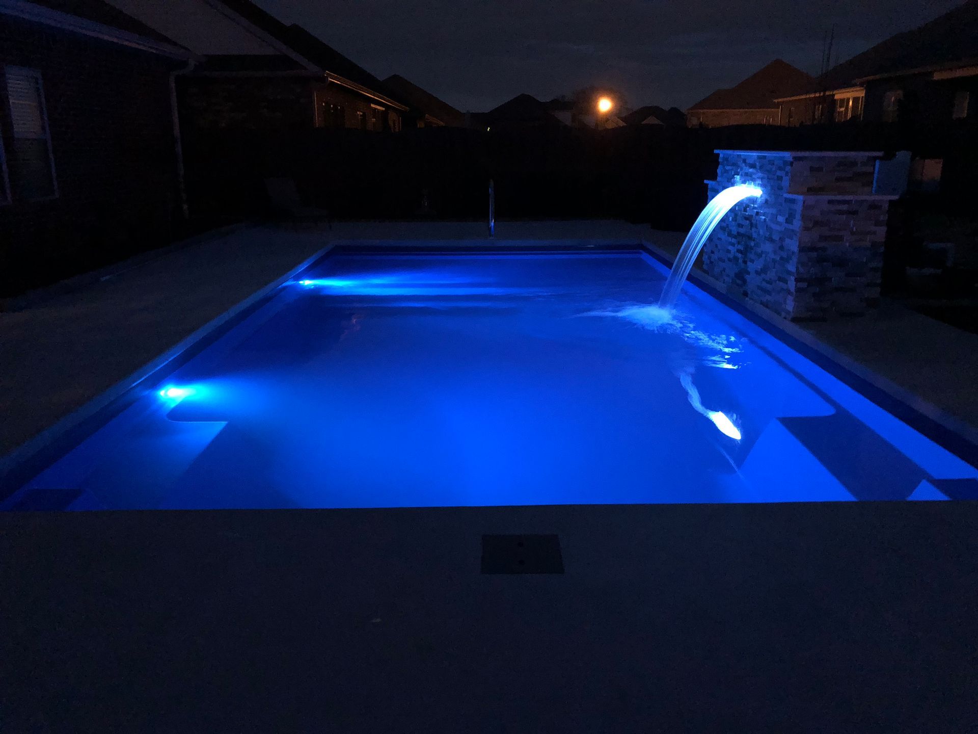 A swimming pool with blue lights and a waterfall at night. - Madison, AL - Valley Pools