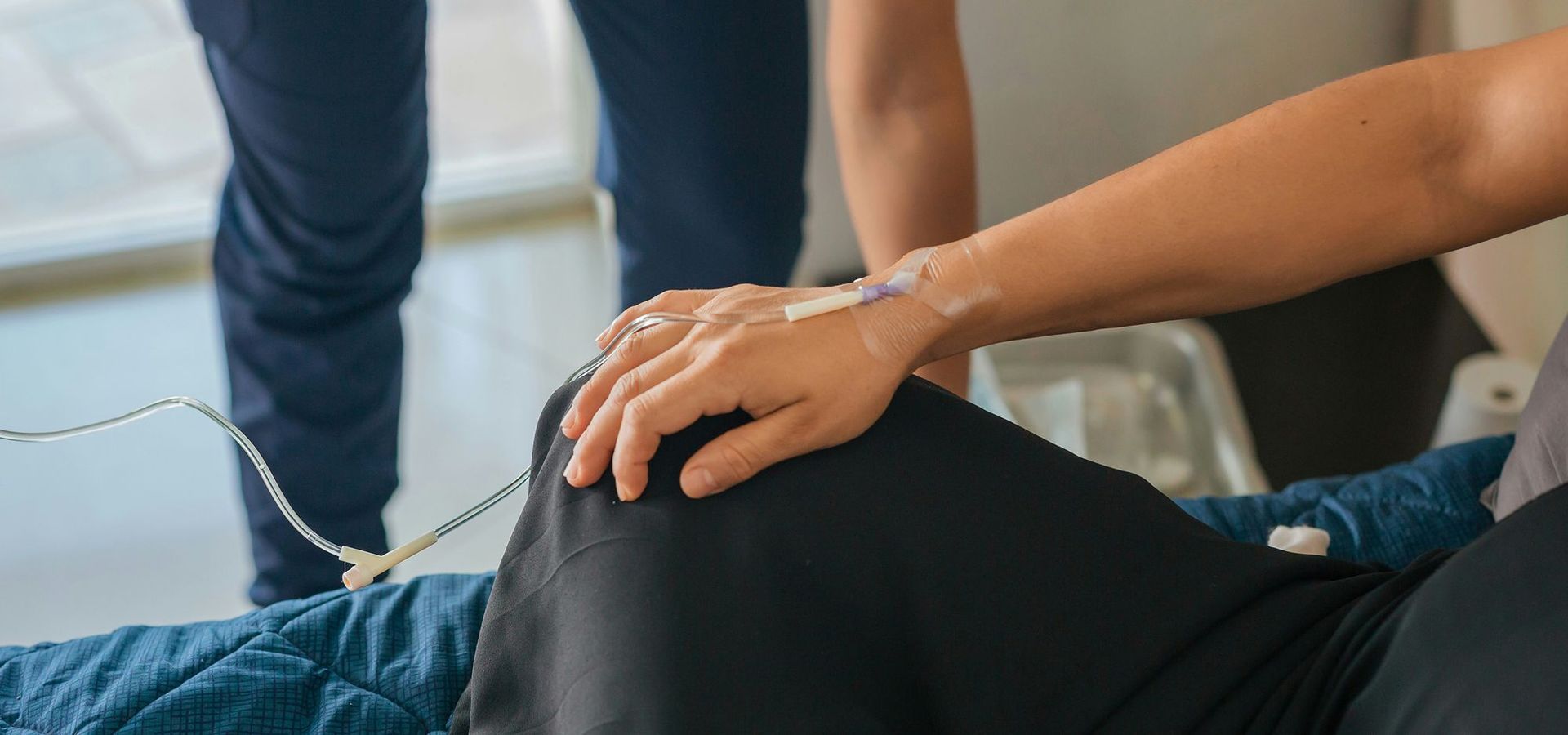 Person receiving IV fluids in a healthcare setting. A healthcare worker is assisting the patient.