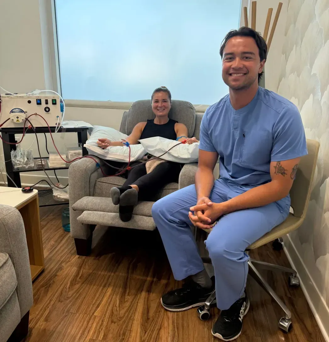 A medical professional smiles beside a patient receiving treatment in a clinic setting.
