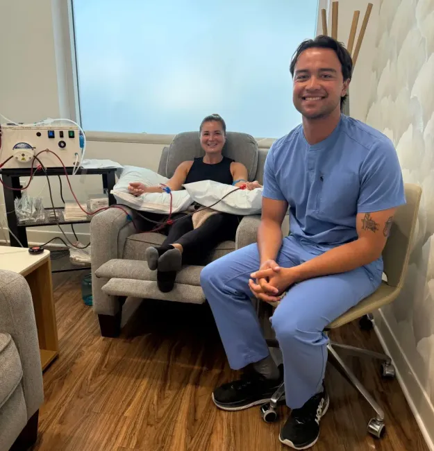 A medical professional smiles beside a patient receiving treatment in a clinic setting.
