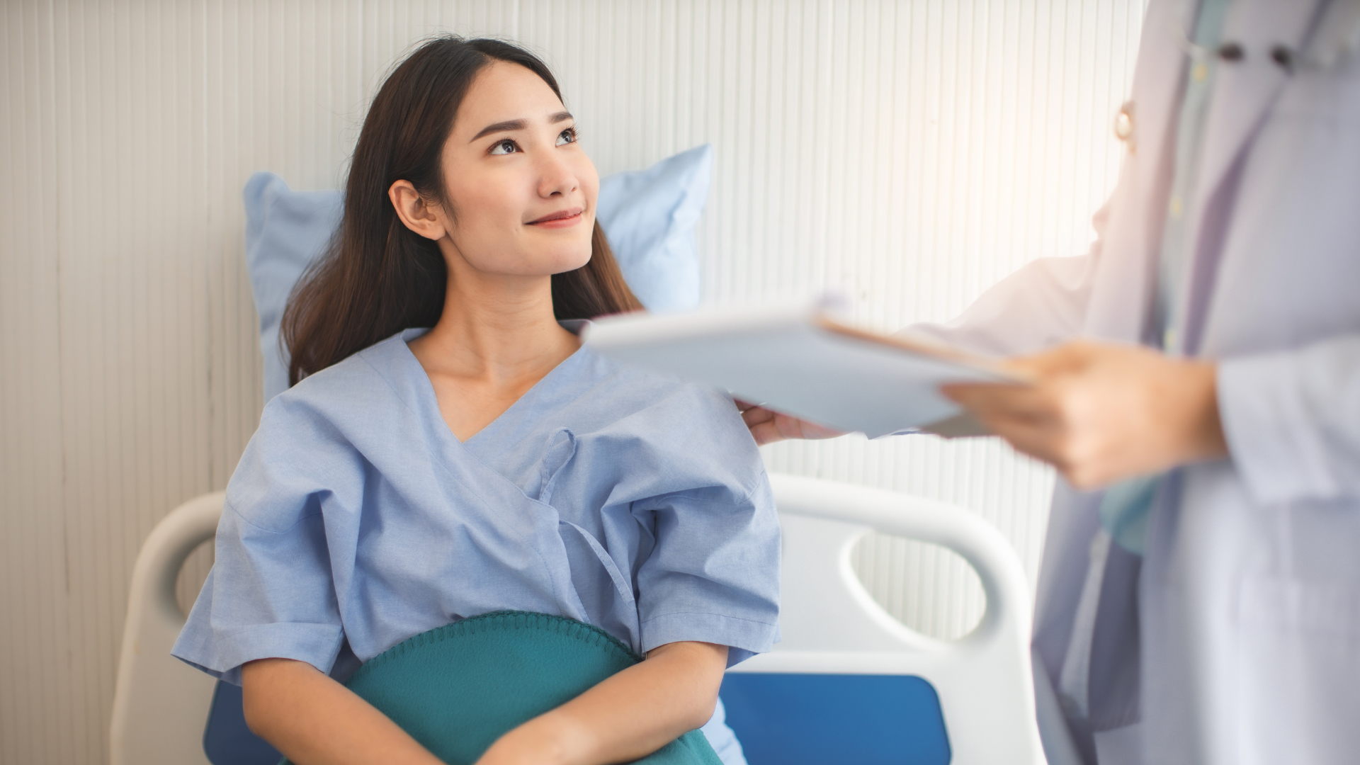 Woman in hospital bed smiles while a doctor shows her a chart.
