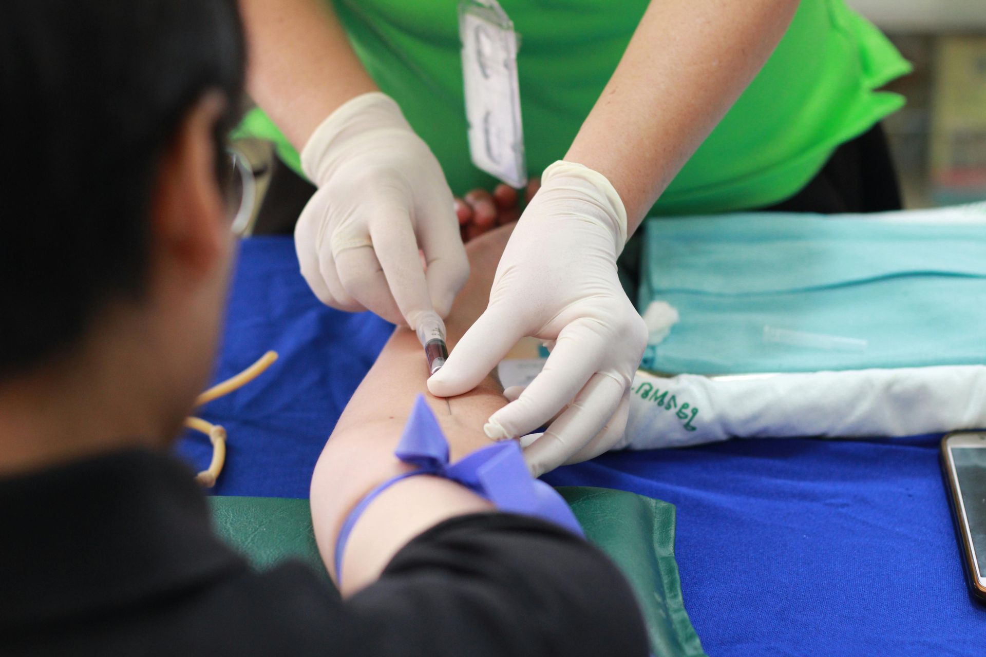 Person having blood drawn at a medical clinic. Hands with gloves, arm with tourniquet, needle inserted.