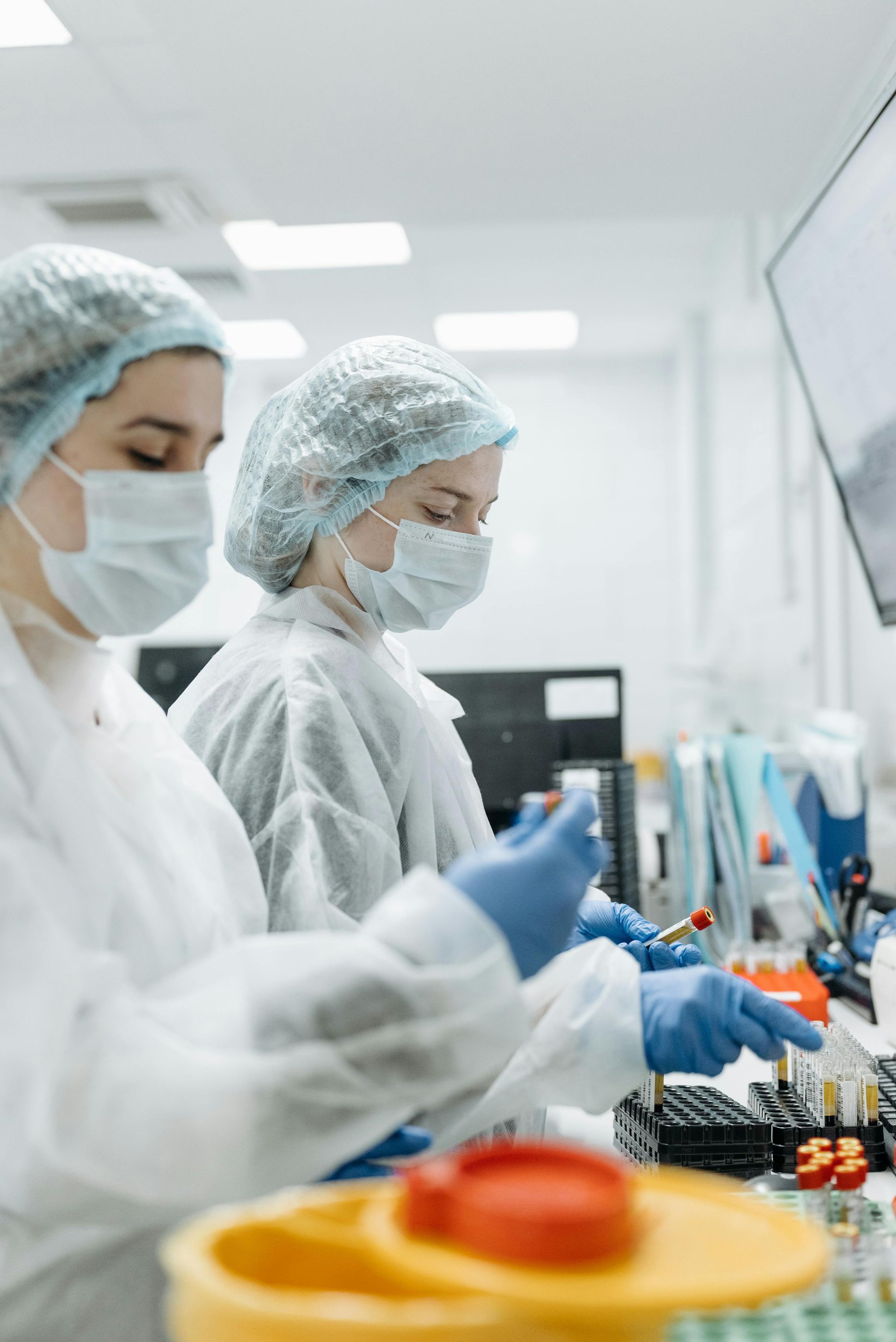Two lab technicians in protective gear work with test tubes.