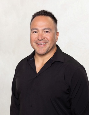 Man in white coat and blue shirt smiles at the camera against a light blue background.