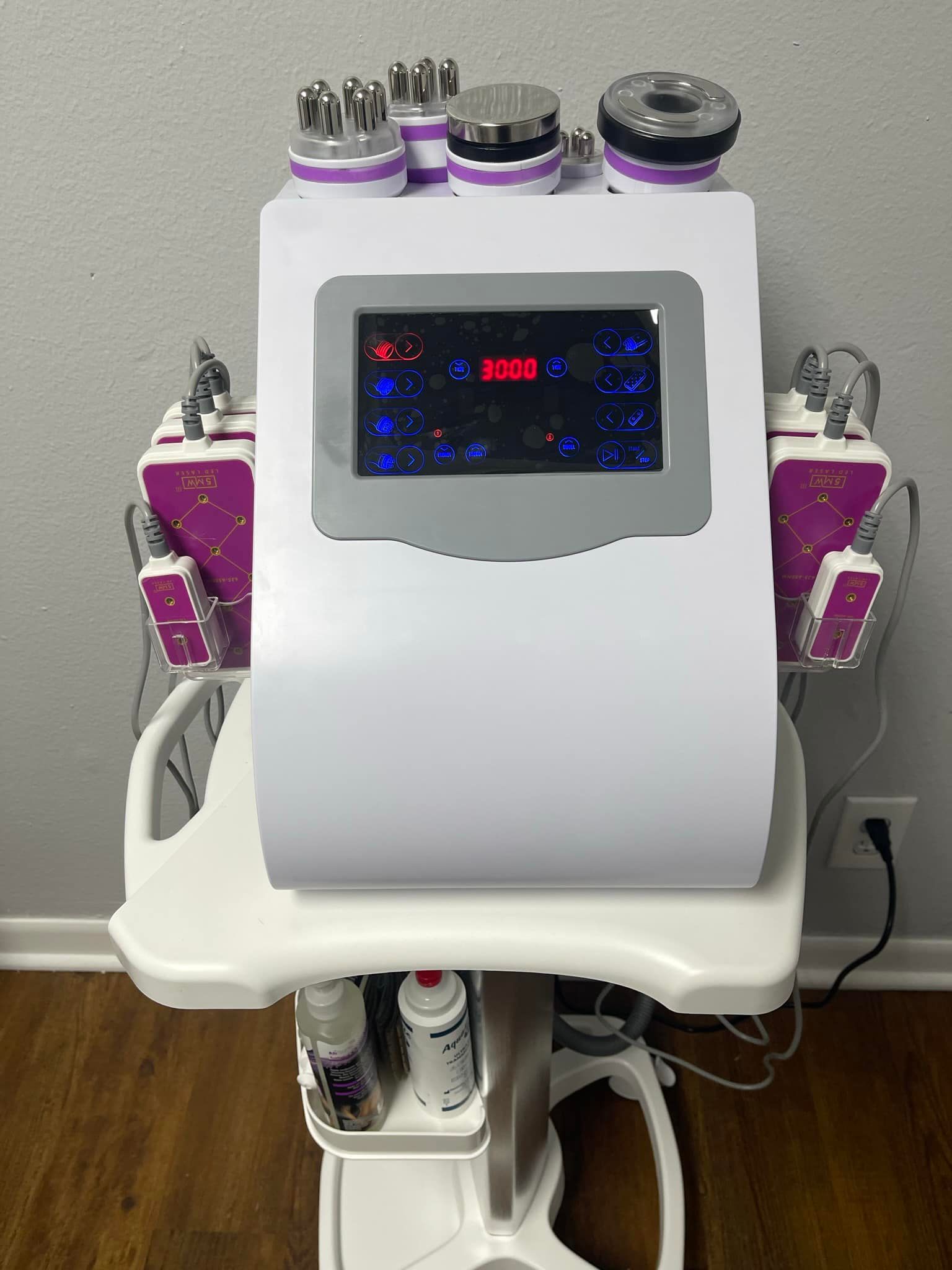 White body contouring machine on a rolling cart with applicators, control panel, and bottles.