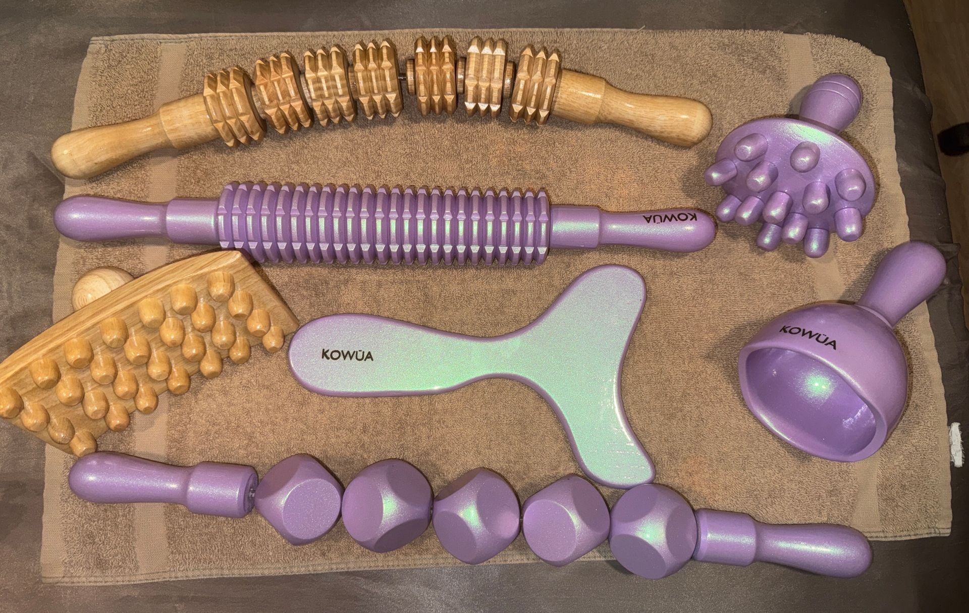 Various massage tools on a towel: wooden rollers, purple handled massage balls and shapes.