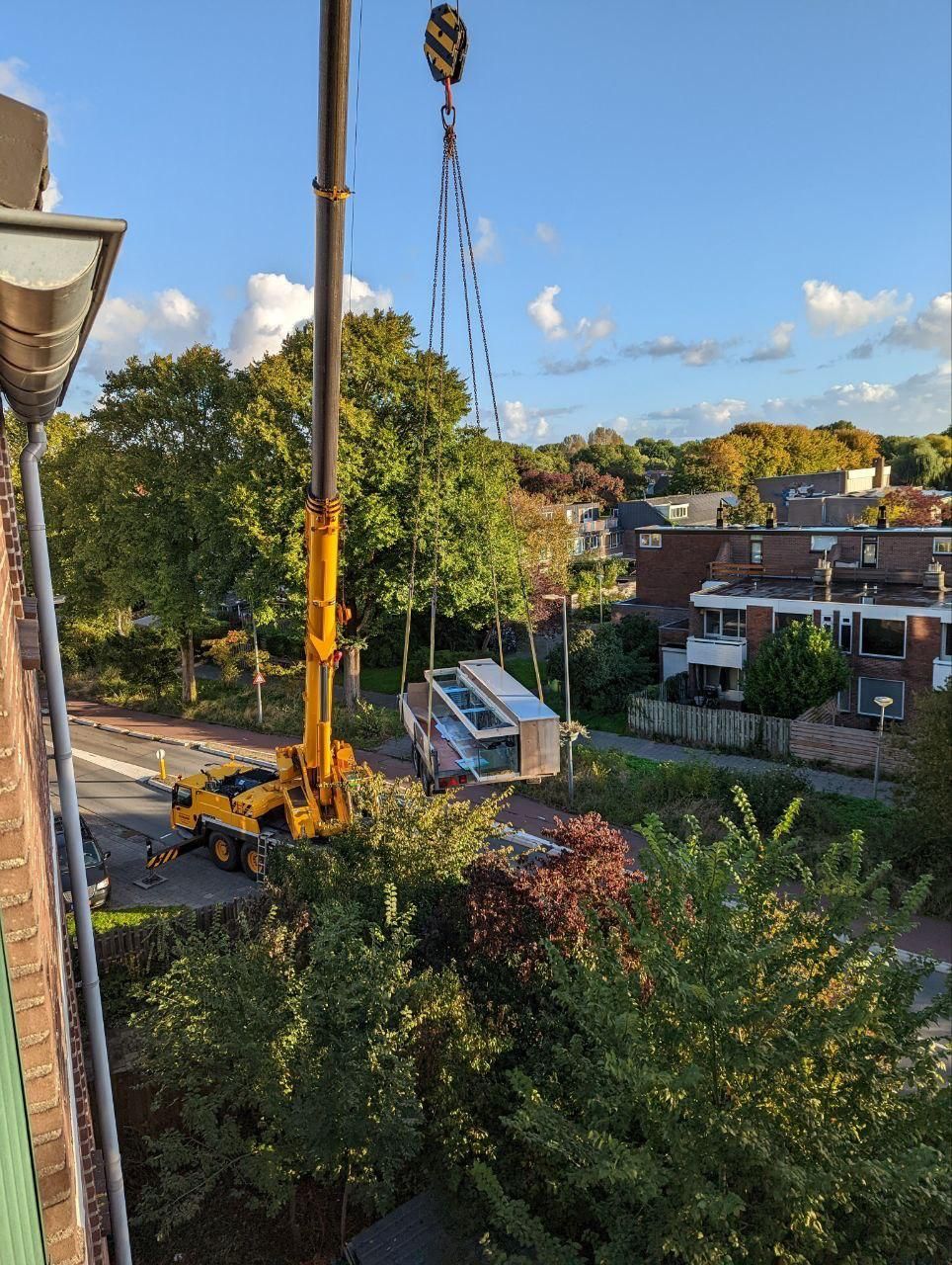 Een kraan tilt een gebouw op in een woonwijk.