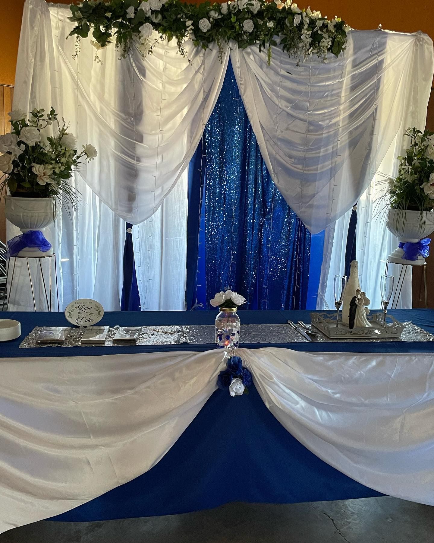 Royal blue and white decorated head table, with floral arrangements and sequin backdrop.