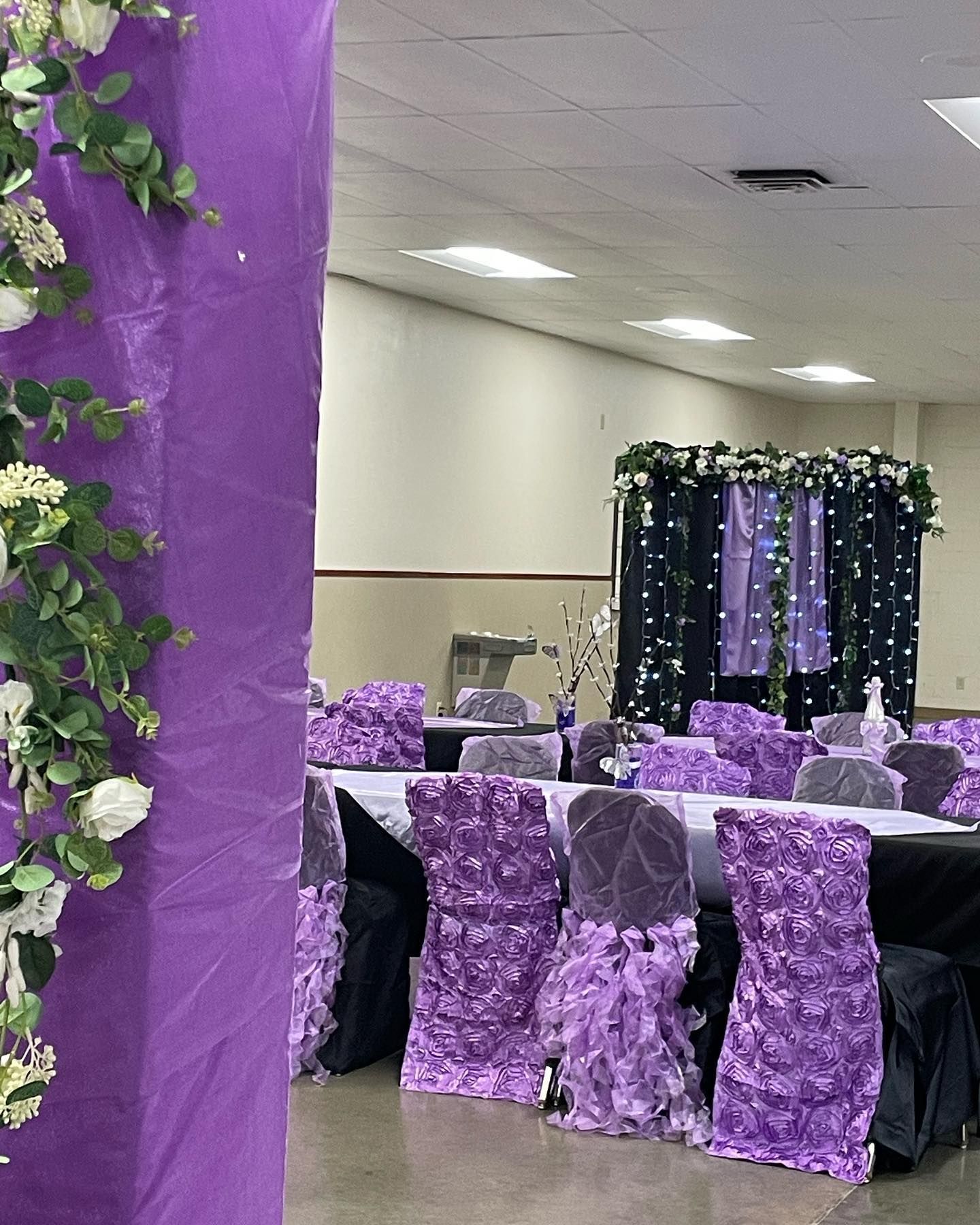 Purple and white decorated event space with draped columns, decorated chairs, and a backdrop.