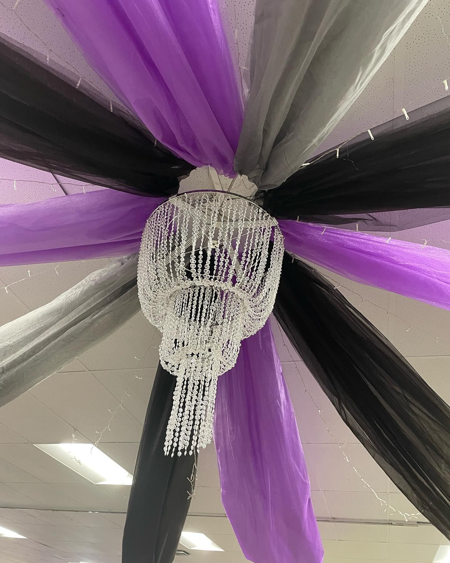 Chandelier surrounded by purple, black, and gray fabric draping from a white ceiling.