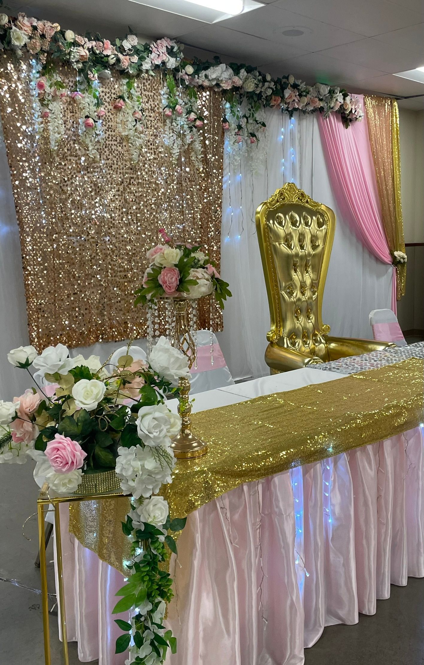 Reception table decorated with pink and gold sequins, flowers, and a gold throne-like chair.