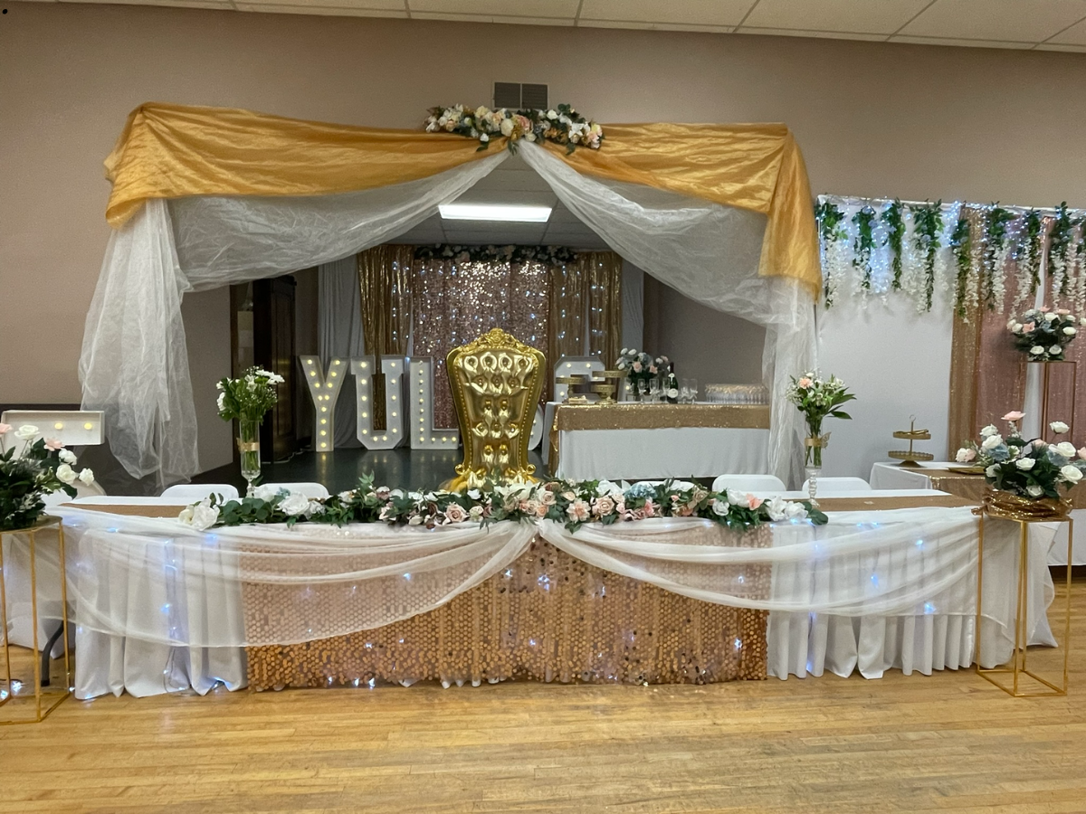 Banquet hall with decorated tables, gold and white decor, floral arrangements, backdrop with