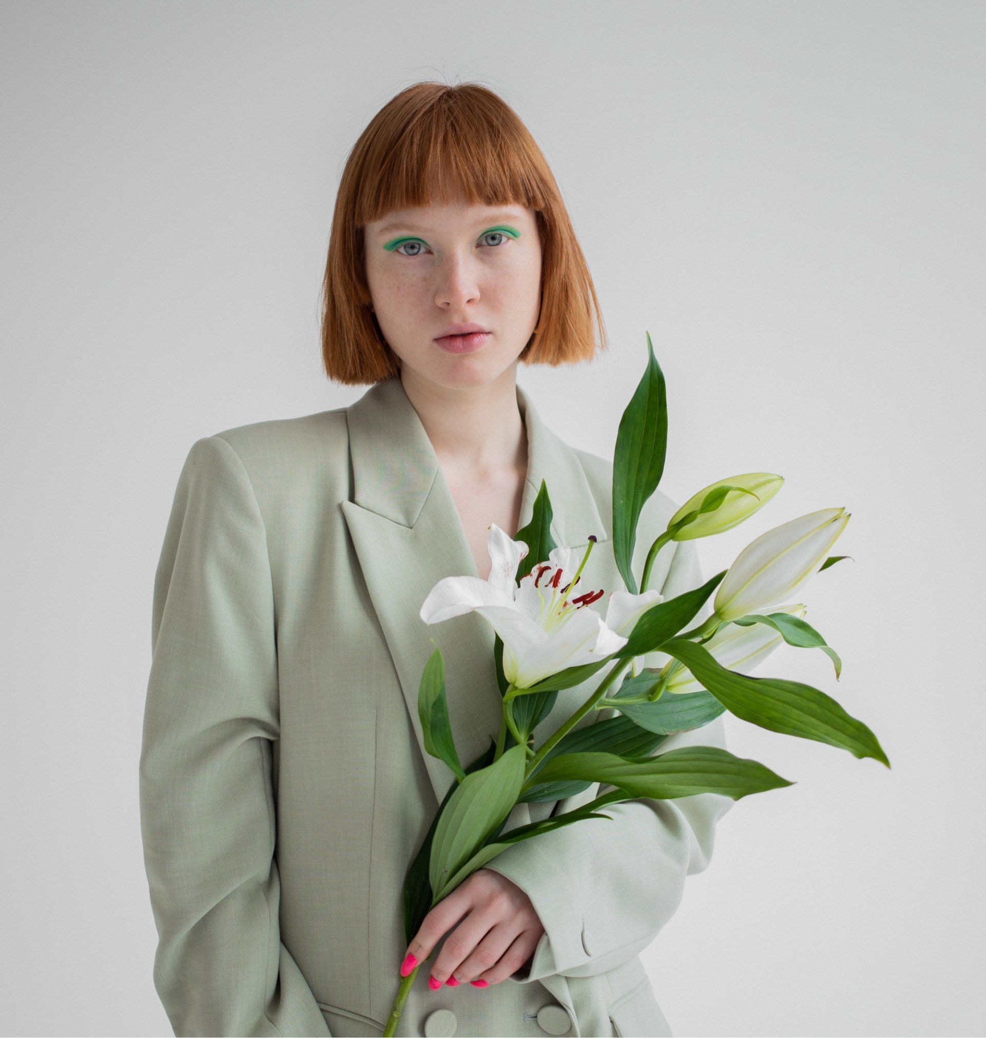 Woman in green blazer with white lilies, looking at the camera. Green eye makeup.