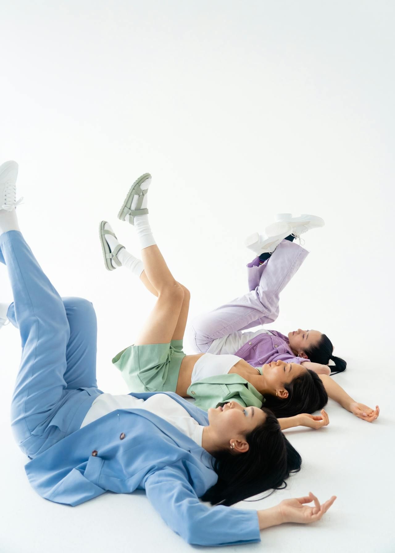 Three people lying on the floor with legs raised in the air. White background; wearing casual clothing.
