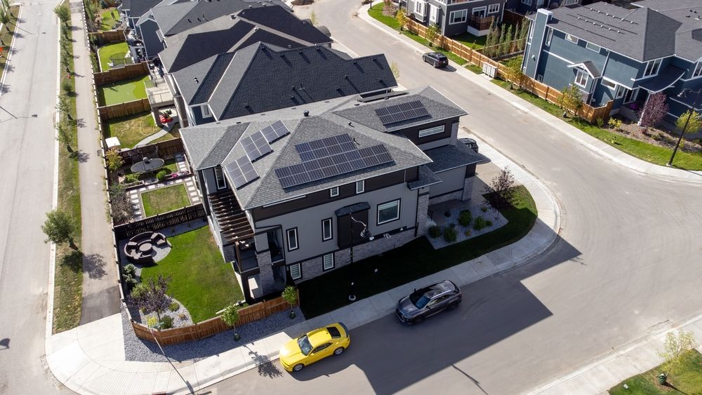 An aerial view of a residential neighborhood with a house with solar panels on the roof.