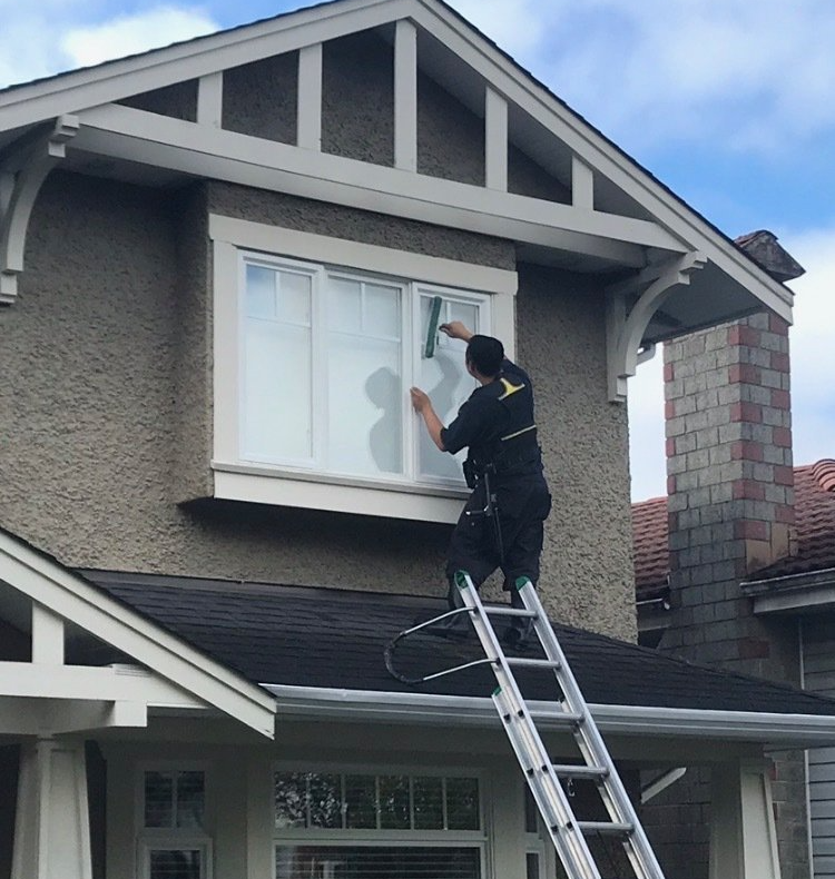 person standing on roof with ladder to clean window