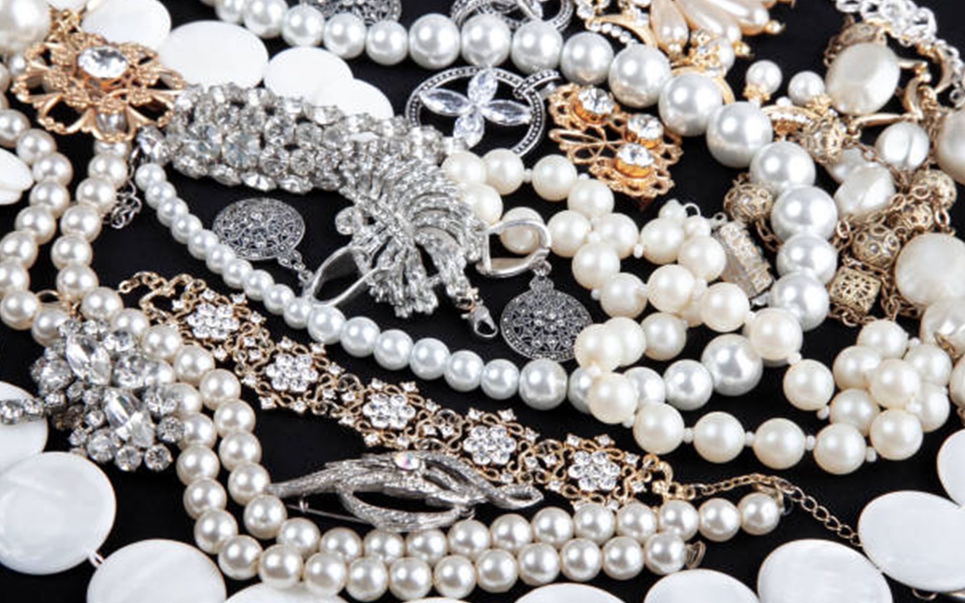 A pile of pearl necklaces and bracelets on a black surface.