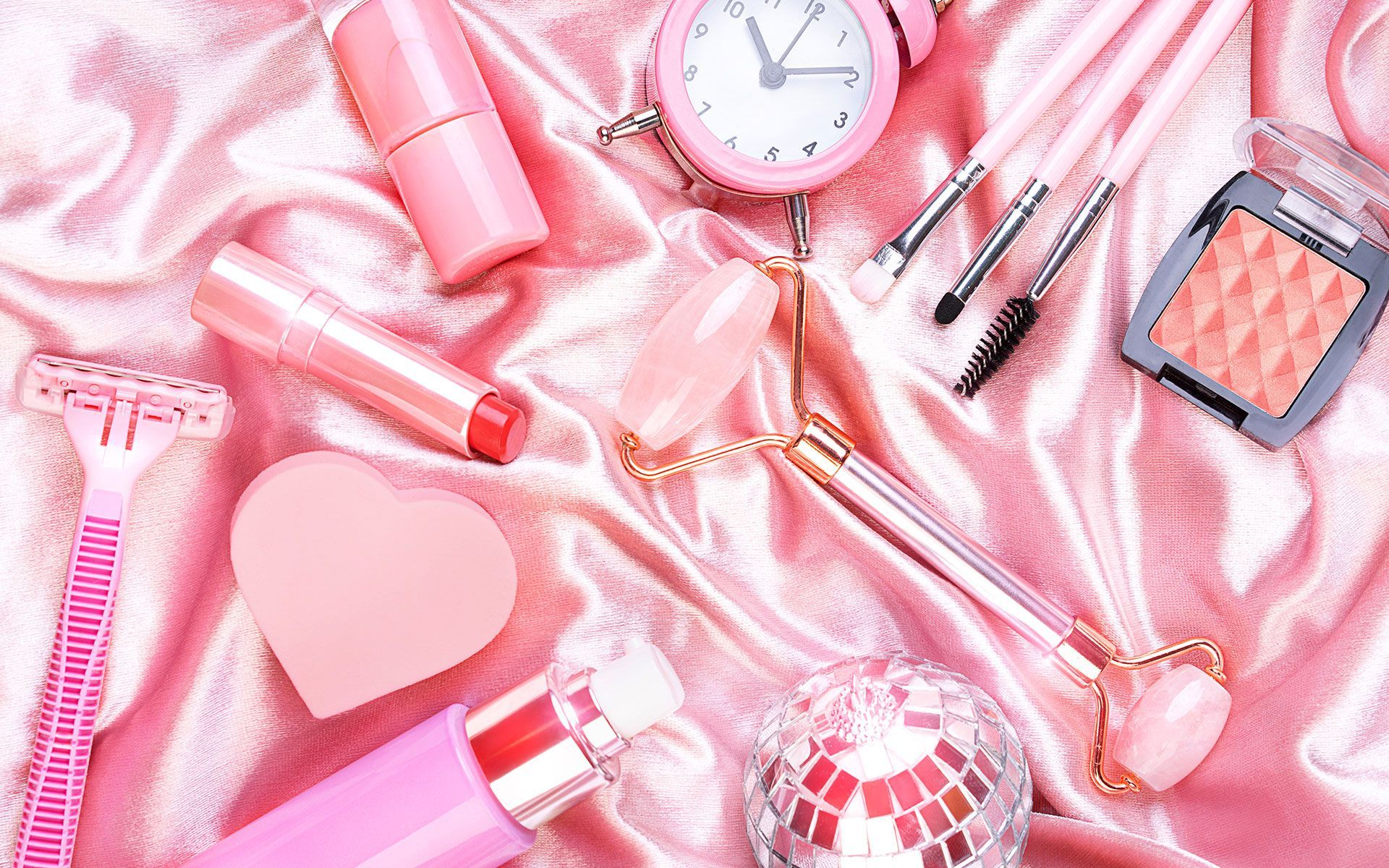 A bunch of pink cosmetics are laying on a pink cloth.